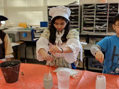 student wearing colonial outfit while making candles
